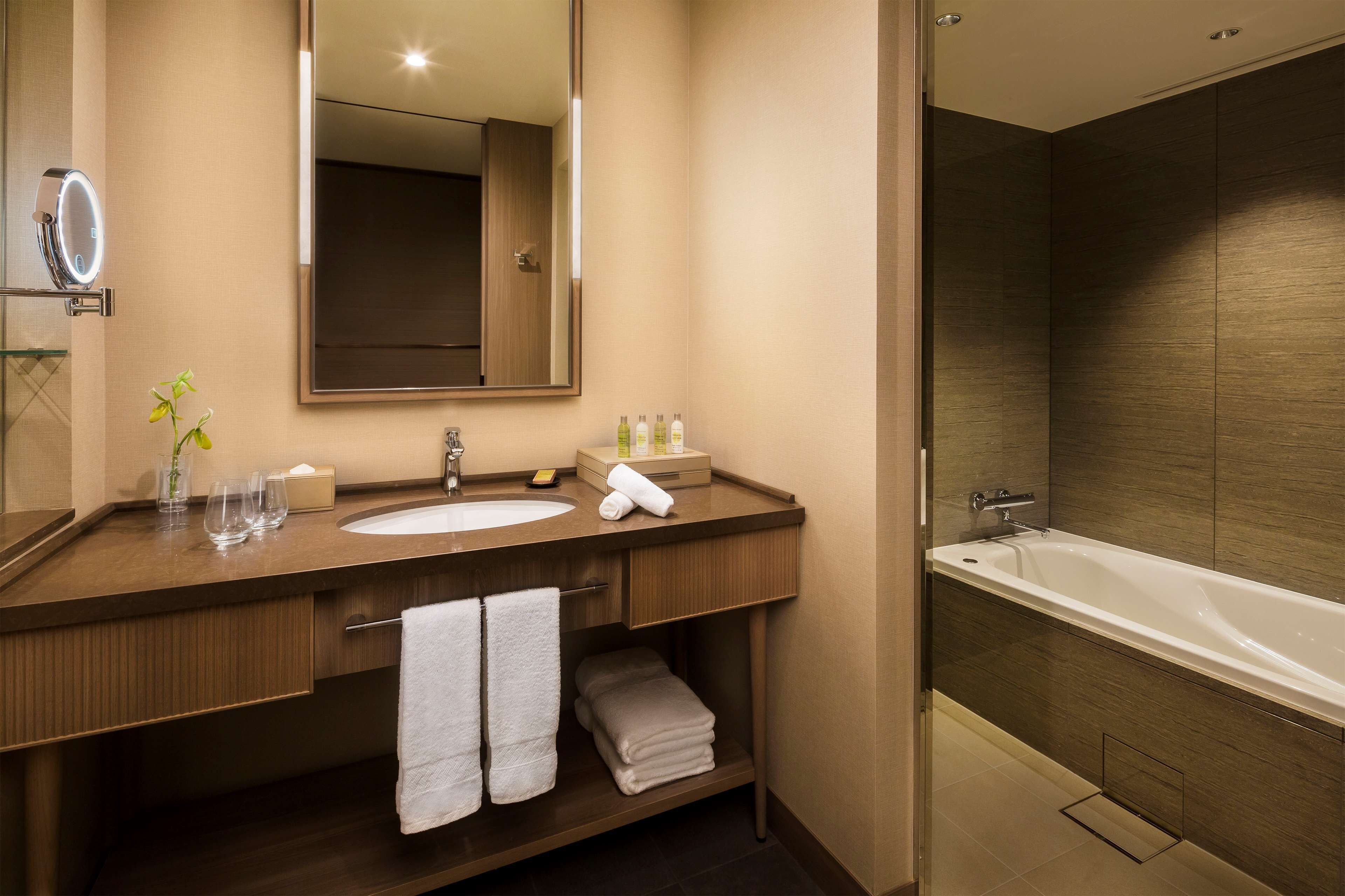 A modern bathroom with a large mirror, a sink, and a bathtub. There are towels and toiletries on the counter.