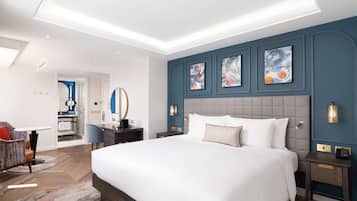 A modern hotel room with a large bed, a desk, a chair, and artwork on the walls.