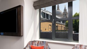 A room with a large window, a television mounted on the wall, and a patterned sofa with red cushions. - Lost Property St. Paul's London, Curio Collection By Hilton (London)