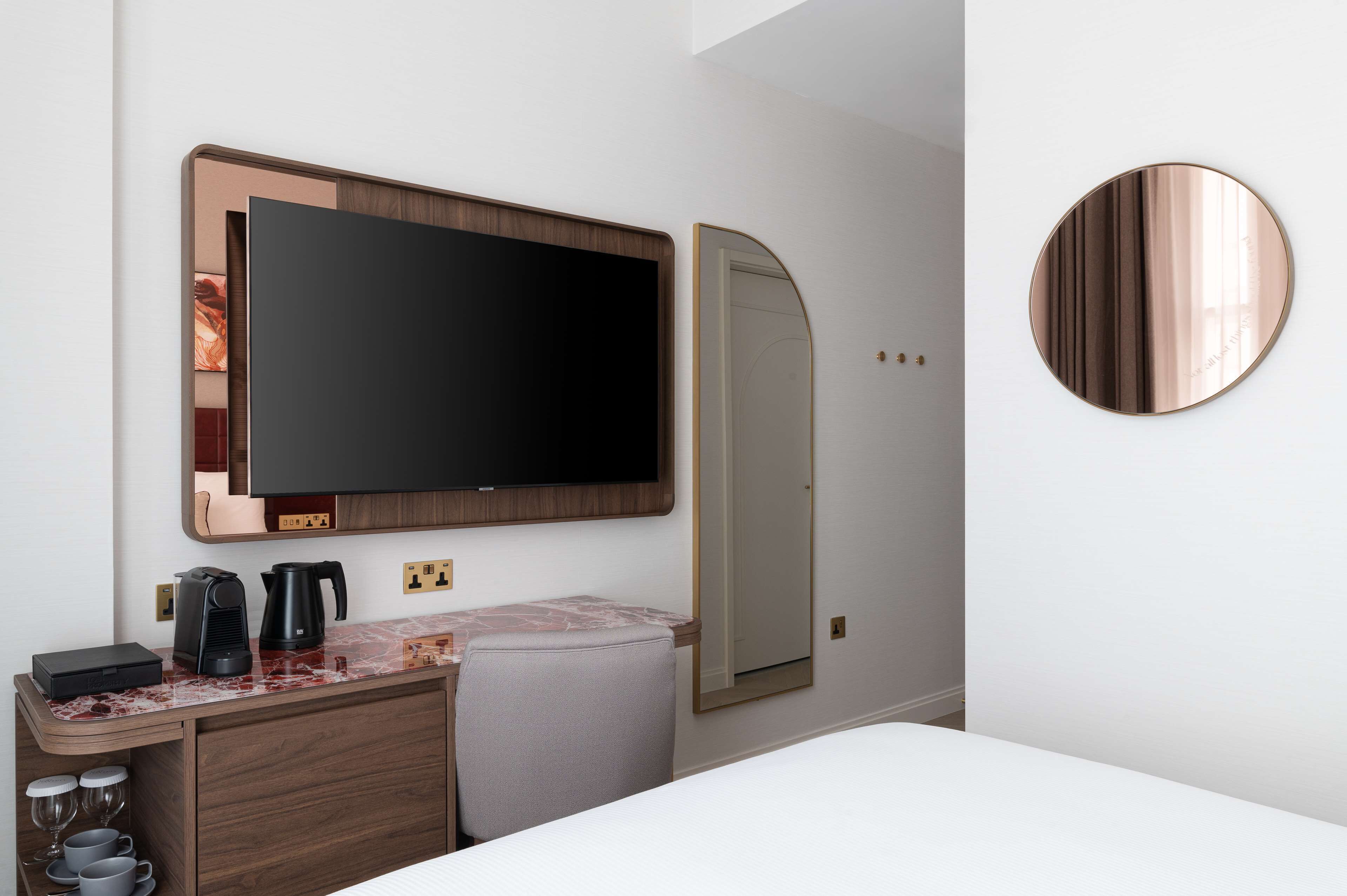 Une chambre d’hôtel équipée d’un téléviseur à écran plat fixé au mur, d’un petit bureau avec une machine à café et d’un miroir.