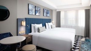 A hotel room with two beds, a round table, a small seating area, and artwork on the wall. - Lost Property St. Paul's London, Curio Collection By Hilton (London)