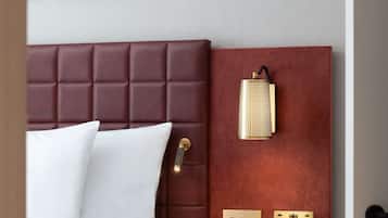 A hotel room with a tufted headboard, a bedside table with a remote control, and a wall-mounted light fixture.