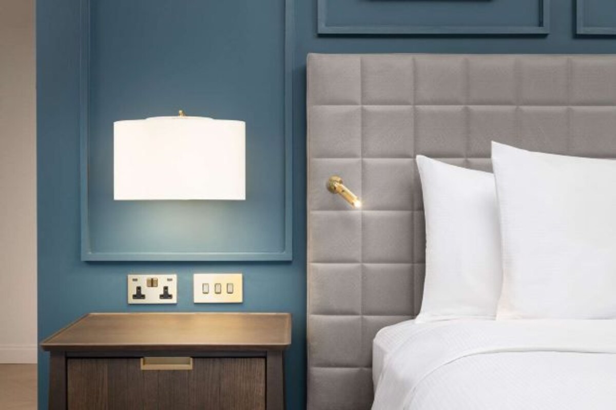 Un dormitorio con cabecera capitonada, mesita de noche y lámpara de pared.