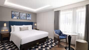 A modern hotel room with a large bed, a chair, a small table, and artwork on the wall.