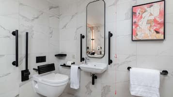 A modern bathroom with a toilet, sink, and mirror. There is a framed artwork on the wall and a towel rack with towels.