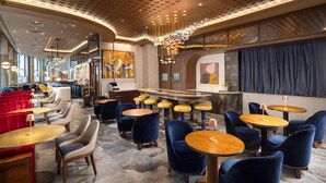 A modern bar area with round tables and blue chairs, a high ceiling with a unique pattern, and a large chandelier. - Lost Property St. Paul's London, Curio Collection By Hilton (London)