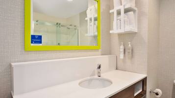 Un baño con un lavamanos blanco, un espejo con marco amarillo y una cabina de ducha de vidrio.