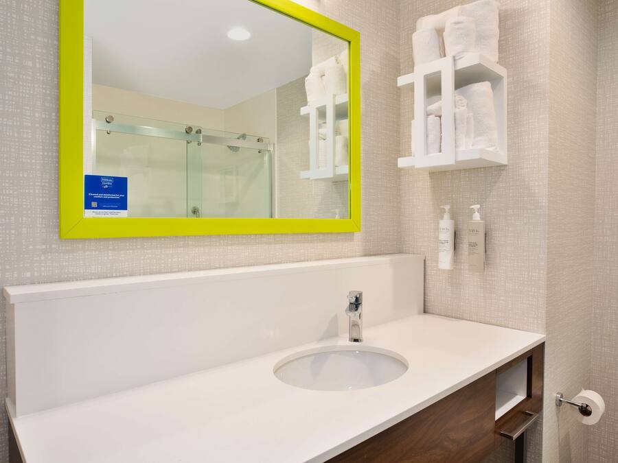 Un baño con un lavamanos blanco, un espejo con marco amarillo y una cabina de ducha de vidrio.