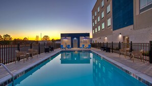 A swimming pool with lounge chairs and umbrellas, surrounded by a fence, and a building with multiple windows in the background. - Hampton Inn By Hilton Paris (Paris)