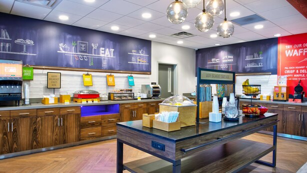 A modern cafe with a wooden counter, a glass display case, and a chalkboard menu on the wall. - Hampton Inn By Hilton Paris (Paris)