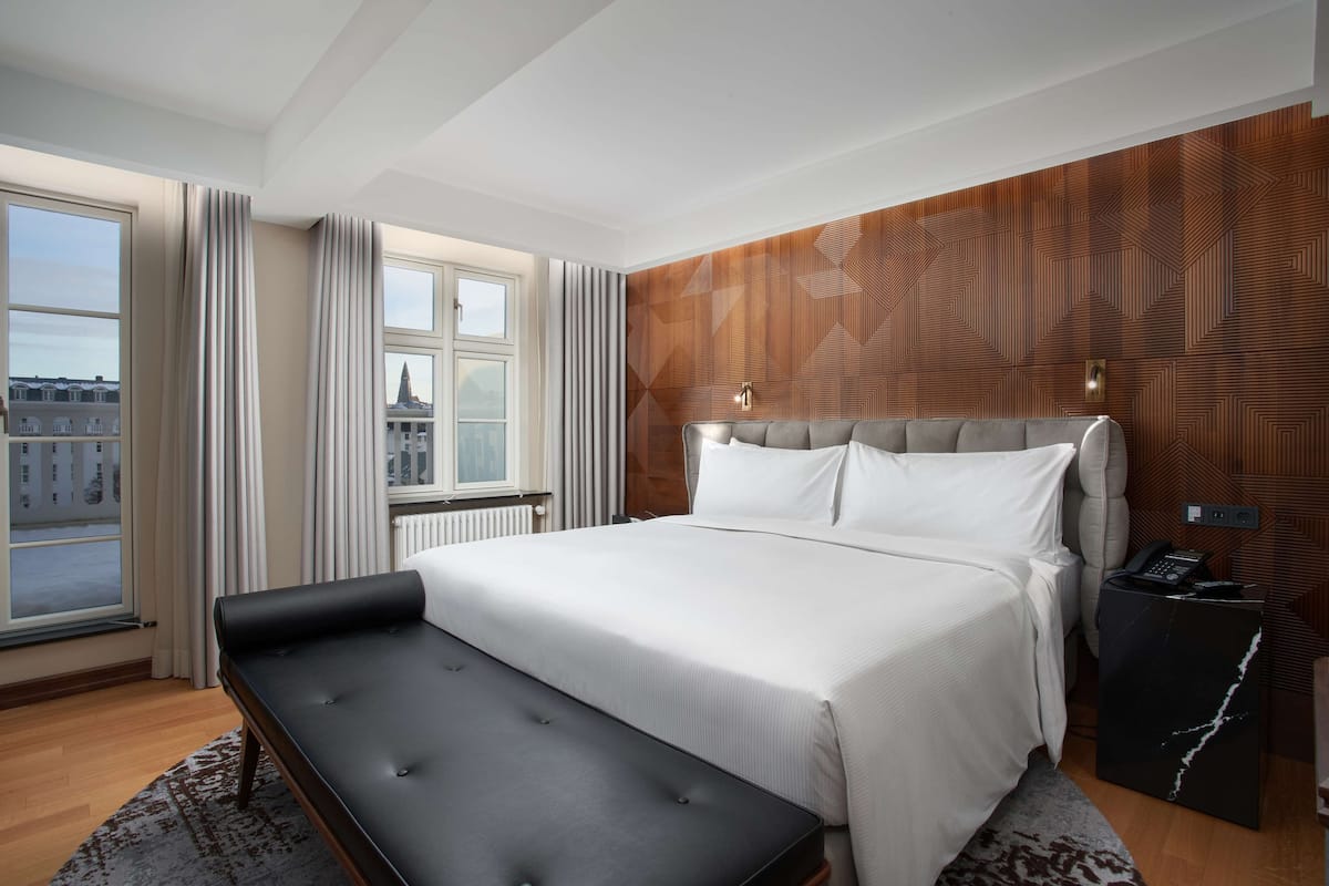 Una habitación de hotel moderna con una cama grande, un banco, una pared de acento de madera y vistas a edificios.