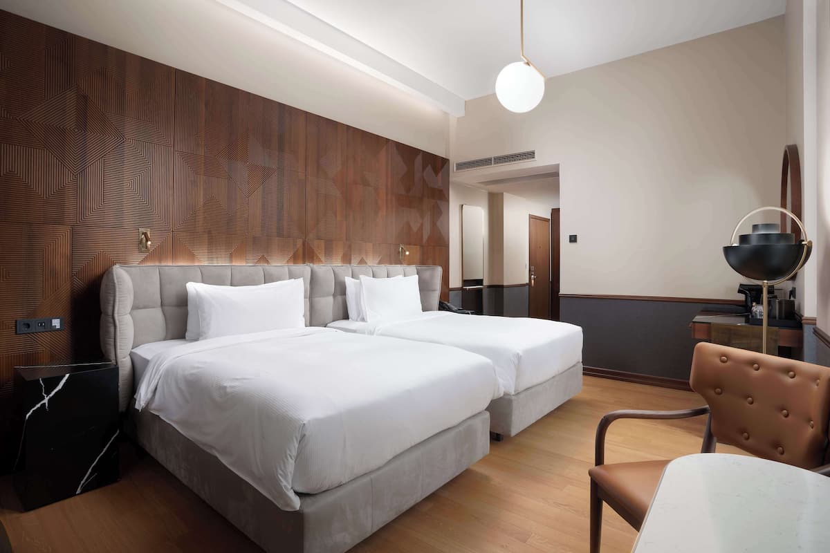 Habitación de hotel con dos camas, una mesa de comedor, una silla y una pared con un diseño geométrico.