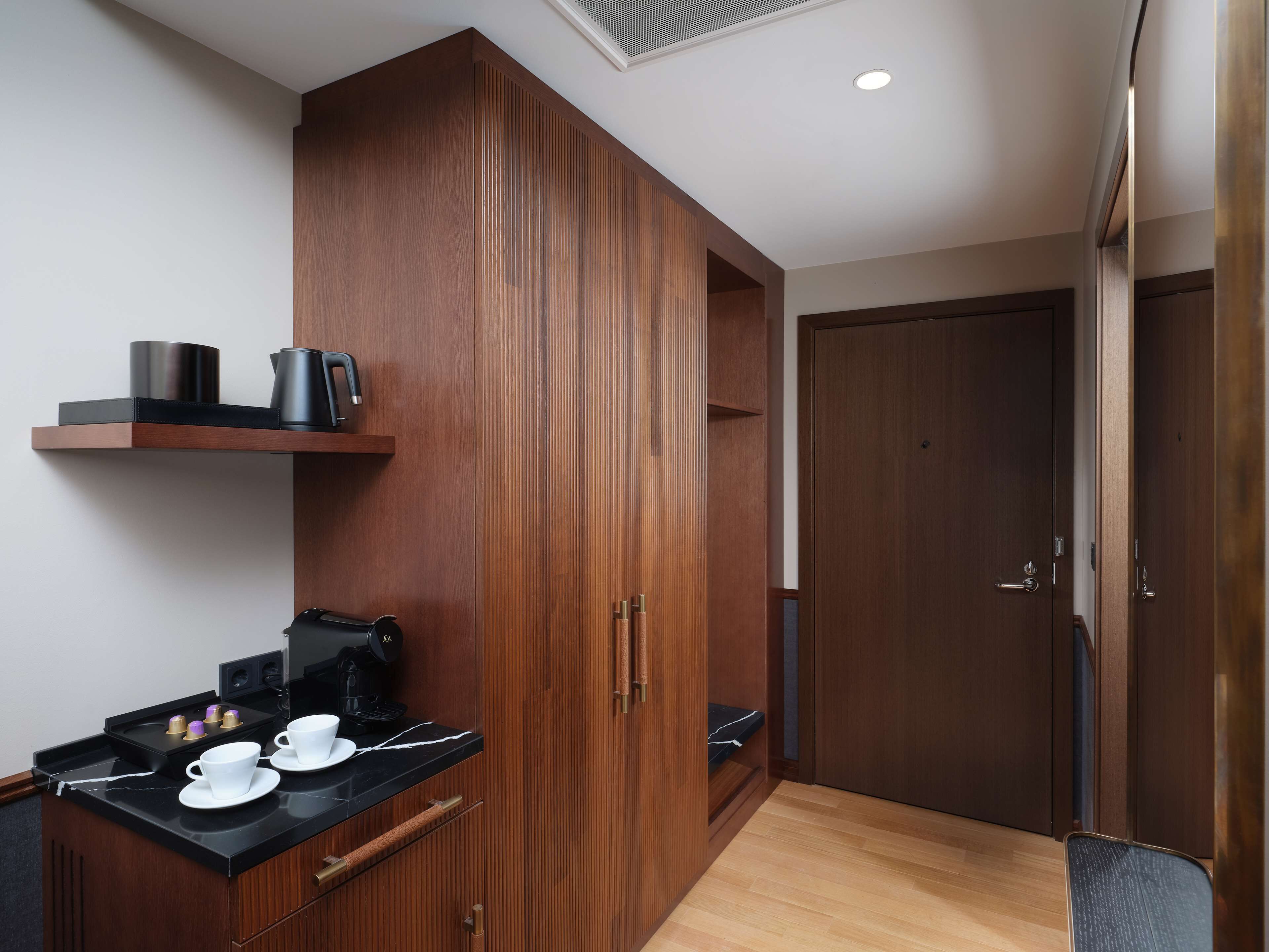 A compact kitchenette with a countertop, a coffee machine, and a small shelf.