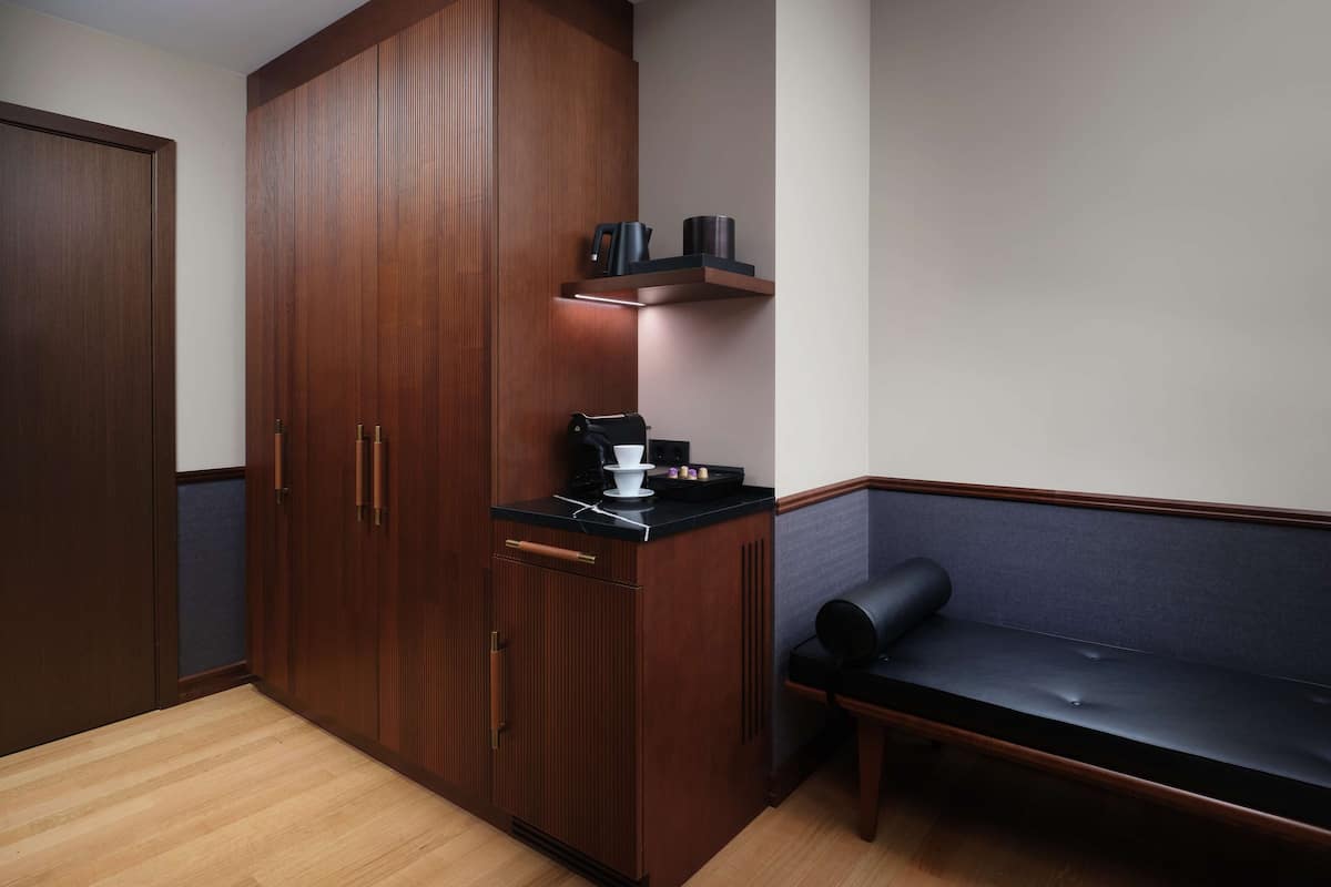 Una habitación compacta con un armario de madera, una encimera negra con cafetera y un banco.