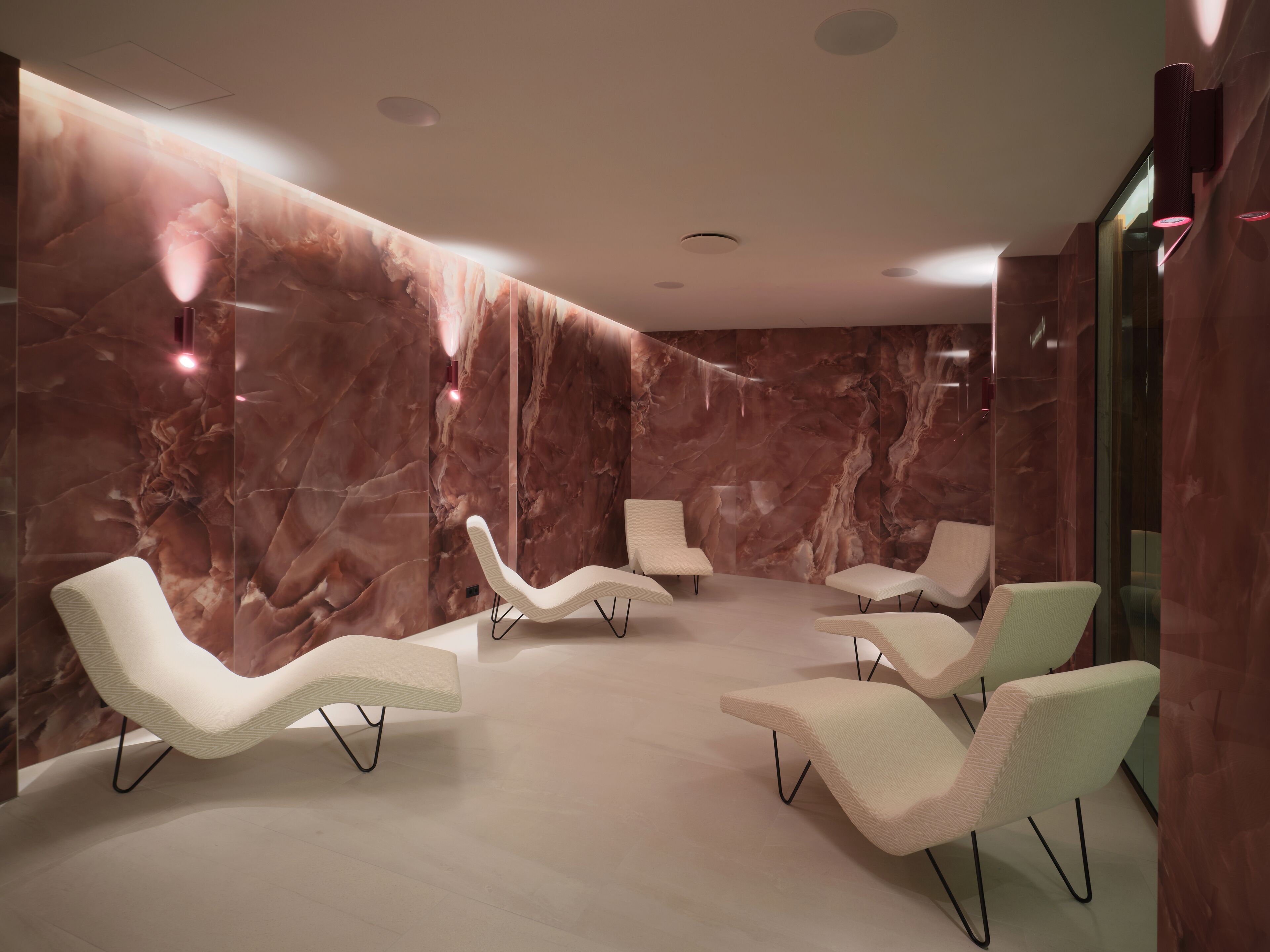 Um lounge moderno com paredes de mármore, várias áreas de estar e iluminação embutida.