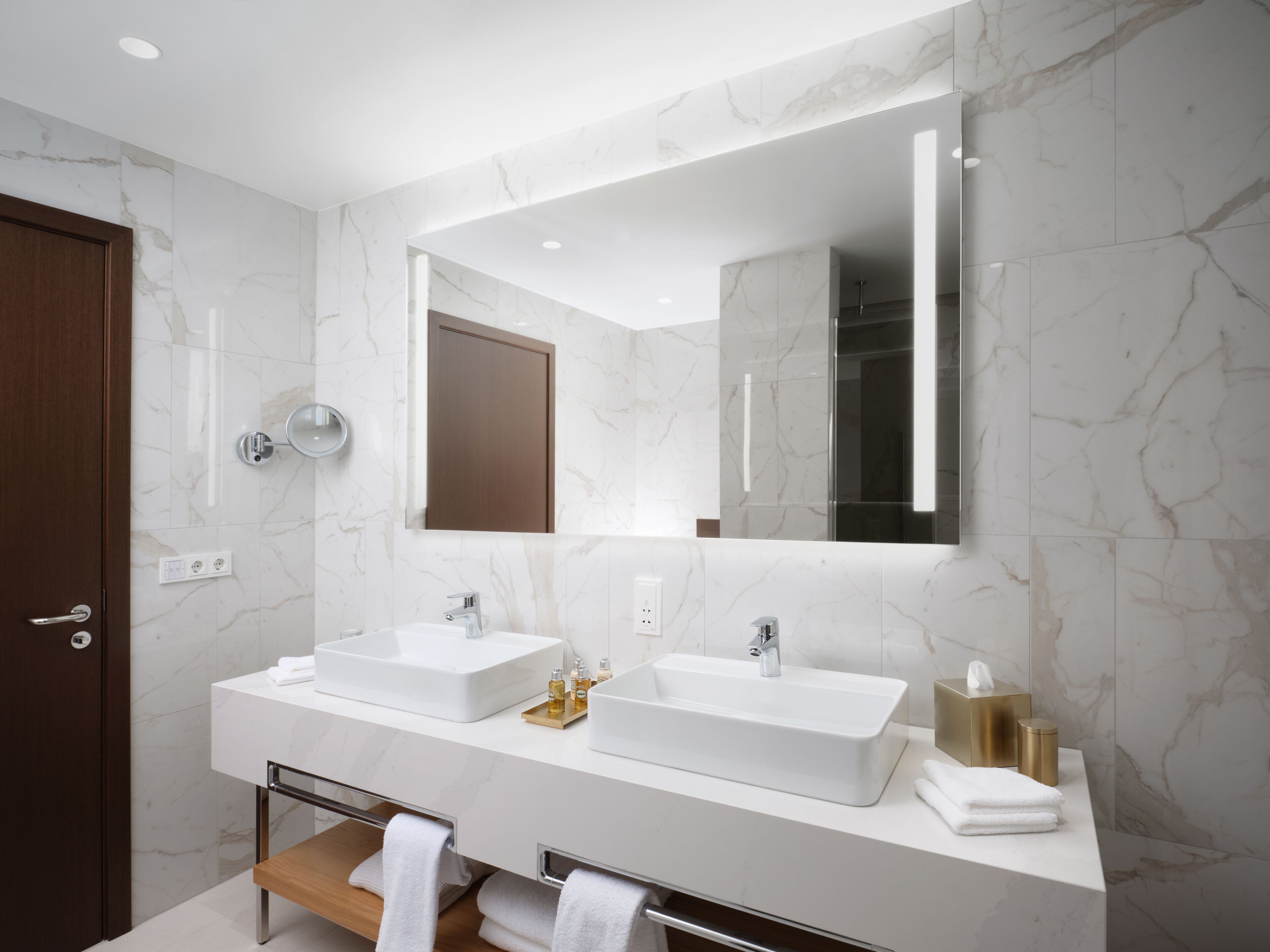 A modern bathroom with two sinks, a large mirror, and a wooden bench.