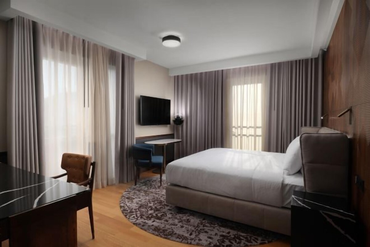 A hotel room with a bed, a desk, a chair, a TV, and curtains.