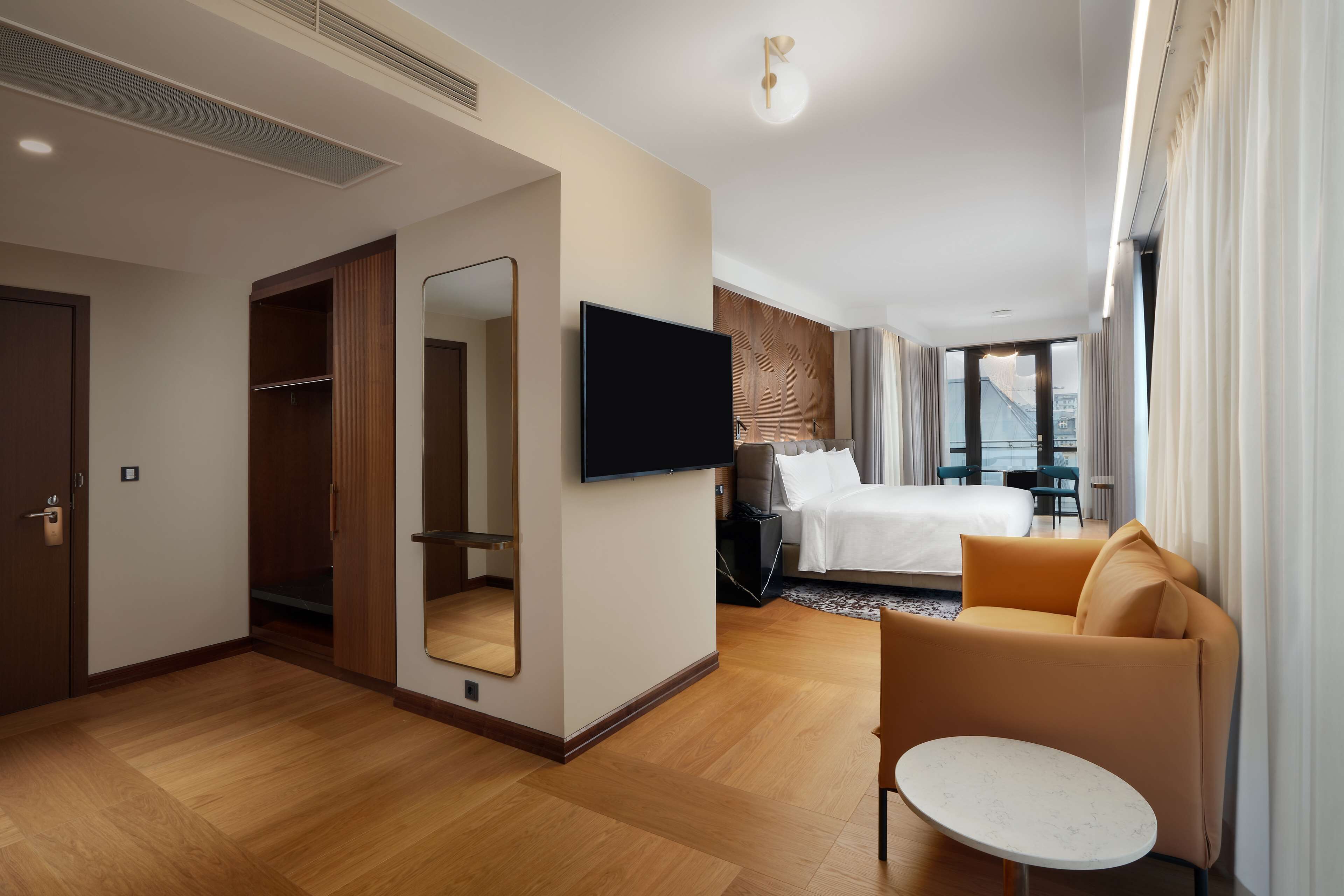 Quarto de hotel com cama, televisão, sofá, mesinha e espelho.