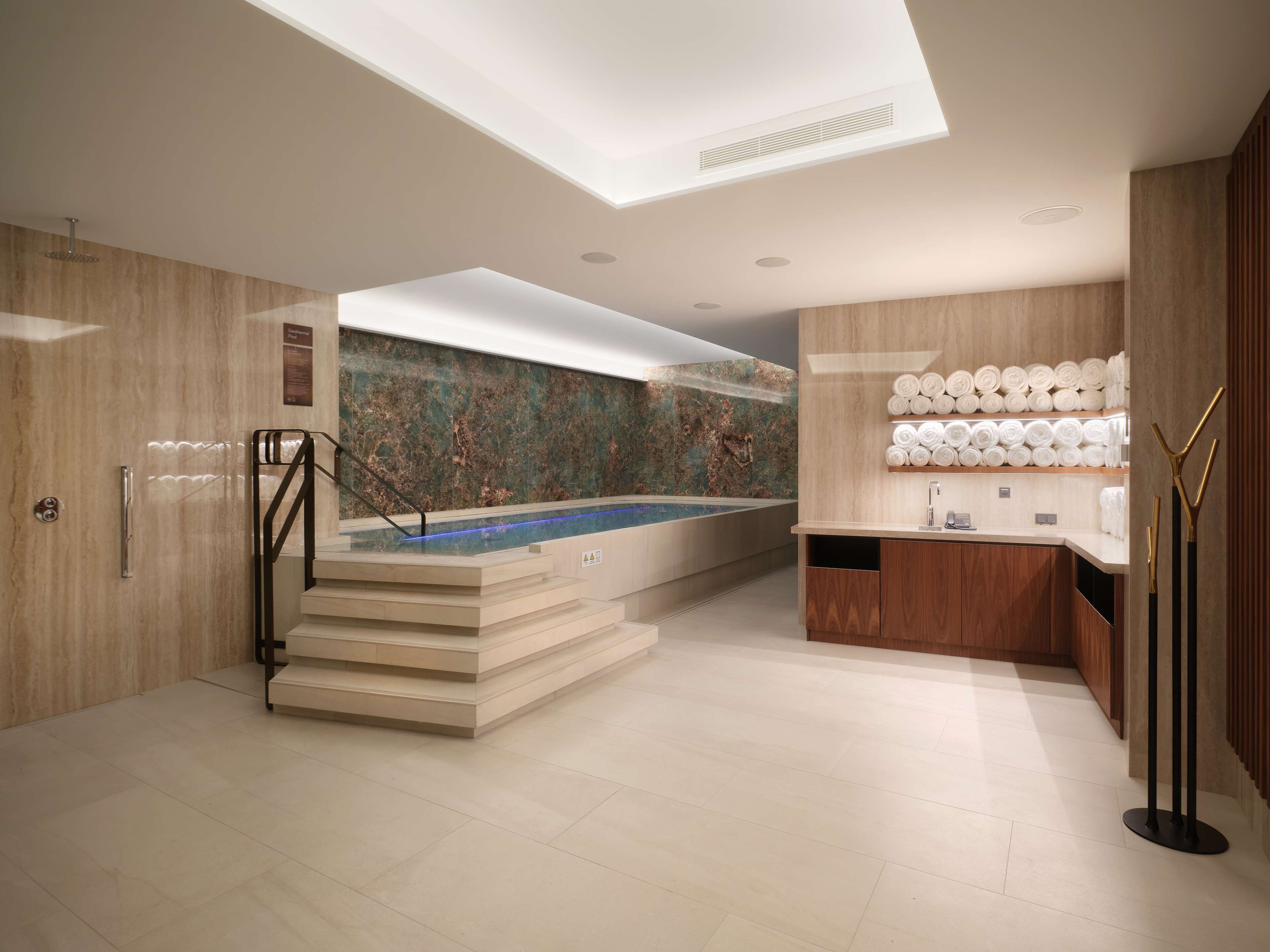 A modern bathroom with a marble wall, a built-in hot tub, and a towel rack.