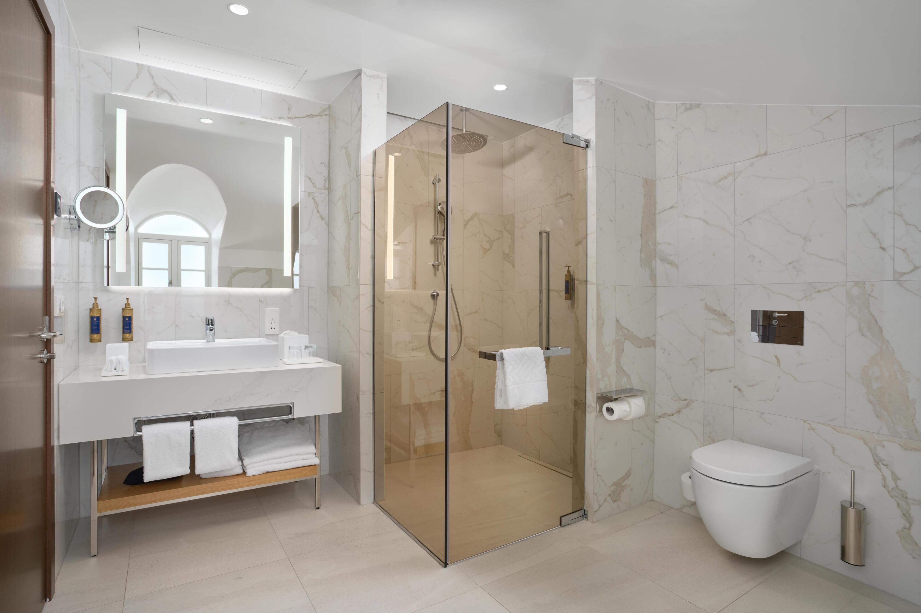A modern bathroom with a glass-enclosed shower, a white sink, and a toilet.