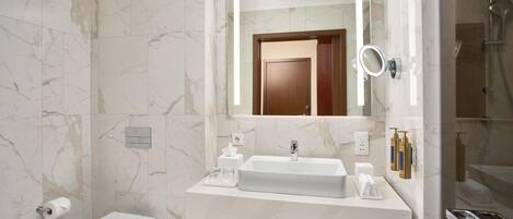 A modern bathroom with a marble wall, a white sink, a toilet, a mirror, and a shower area.