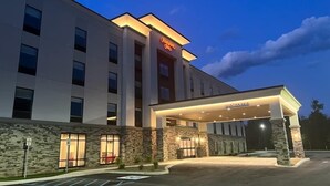 A modern hotel with a stone facade, a well-lit entrance, and a clear view of the parking area.