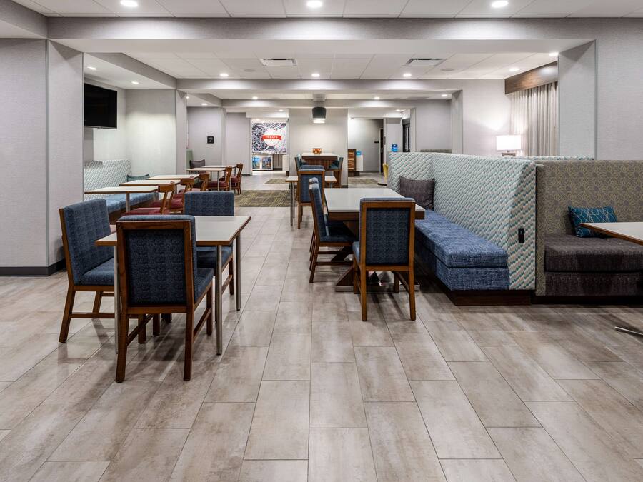 A hotel dining area with tables and chairs, a sofa, and a television on the wall.