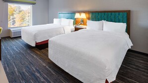A hotel room with two beds, a large window, a wall-mounted lamp, and a patterned headboard.