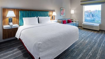 Habitación de hotel con una cama grande, dos mesitas de noche con lámparas, una ventana con vistas y un cabecero con estampado azul.