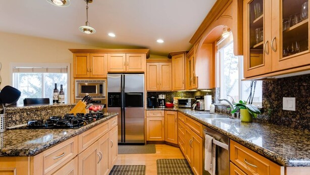A modern kitchen with granite countertops, stainless steel appliances, wooden cabinets, and a large window providing natural light.