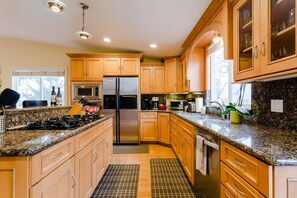 Cocina moderna con encimeras de granito, electrodomésticos de acero inoxidable, armarios de madera y un amplio ventanal que proporciona luz natural.