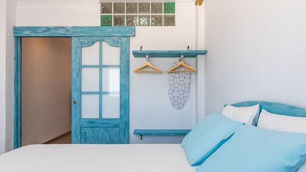 A bedroom with a bed, a door, a wall-mounted shelf with hangers, and a decorative item. - Apartment El Cotarro B  (Vejer de la Frontera)