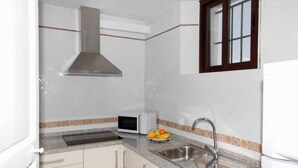 Una cocina equipada con microondas, lavamanos y ventana con persianas.