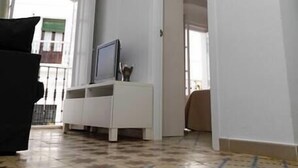 Un'ampia zona giorno con pavimento piastrellato, un mobile TV bianco e un ingresso che dà su un'altra stanza.