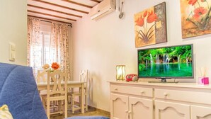 A living room with a television, a dining table with chairs, a blue sofa, and a cabinet with drawers. - Apartamento El Cotarro B (Vejer de la Frontera)