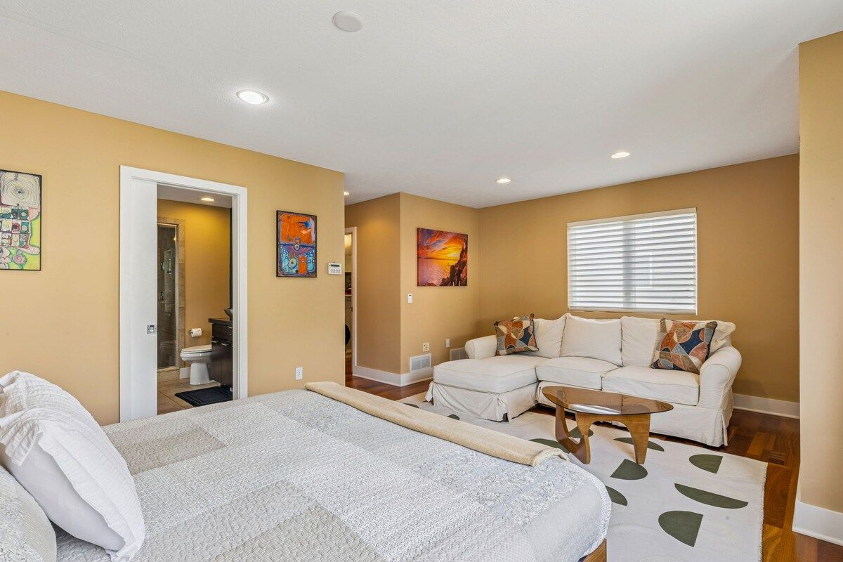 A hotel room with a bed, a sofa, a coffee table, and artwork on the walls.