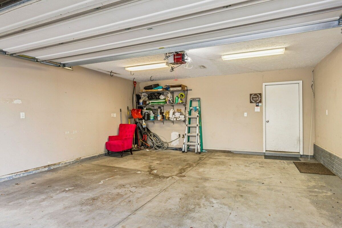 A garage with a concrete floor, a red chair, a ladder, and shelves with various items.