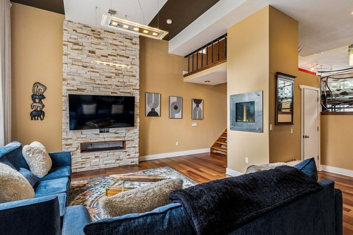 A living room with a stone fireplace, a flat-screen TV, and a staircase leading to an upper level.