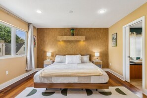 A bedroom with a large bed, wooden headboard, bedside lamps, and a view of the outside.