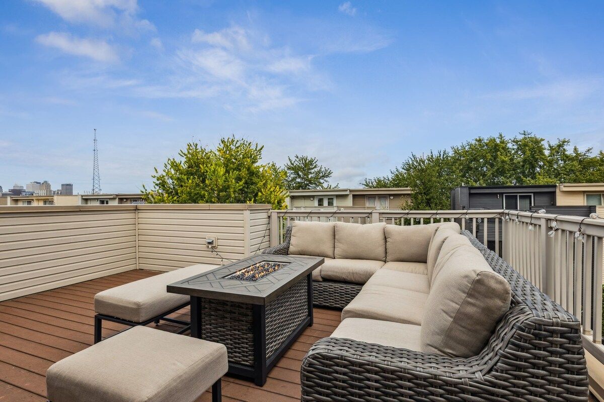 An outdoor deck with a sofa, ottoman, and a fire pit.