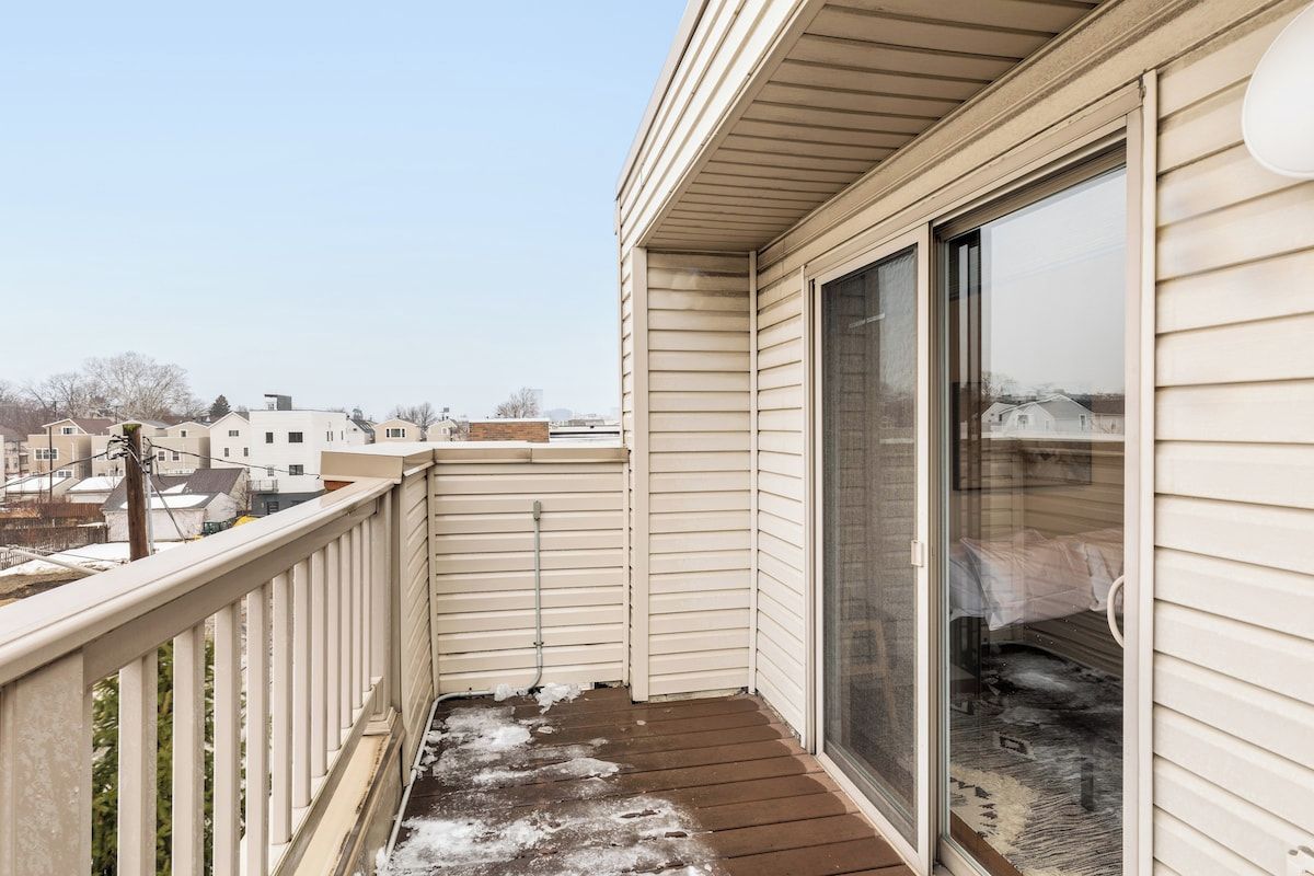 A balcony with a wooden floor, a glass door, and a view of neighboring houses.