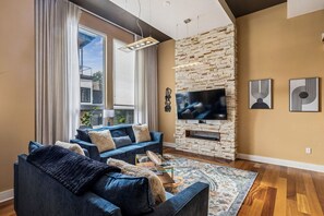 A modern living room with a large flat-screen TV, a blue sofa set, a patterned rug, and a stone accent wall.