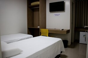 A bedroom with two single beds, a desk with a chair, a television, and a small refrigerator.