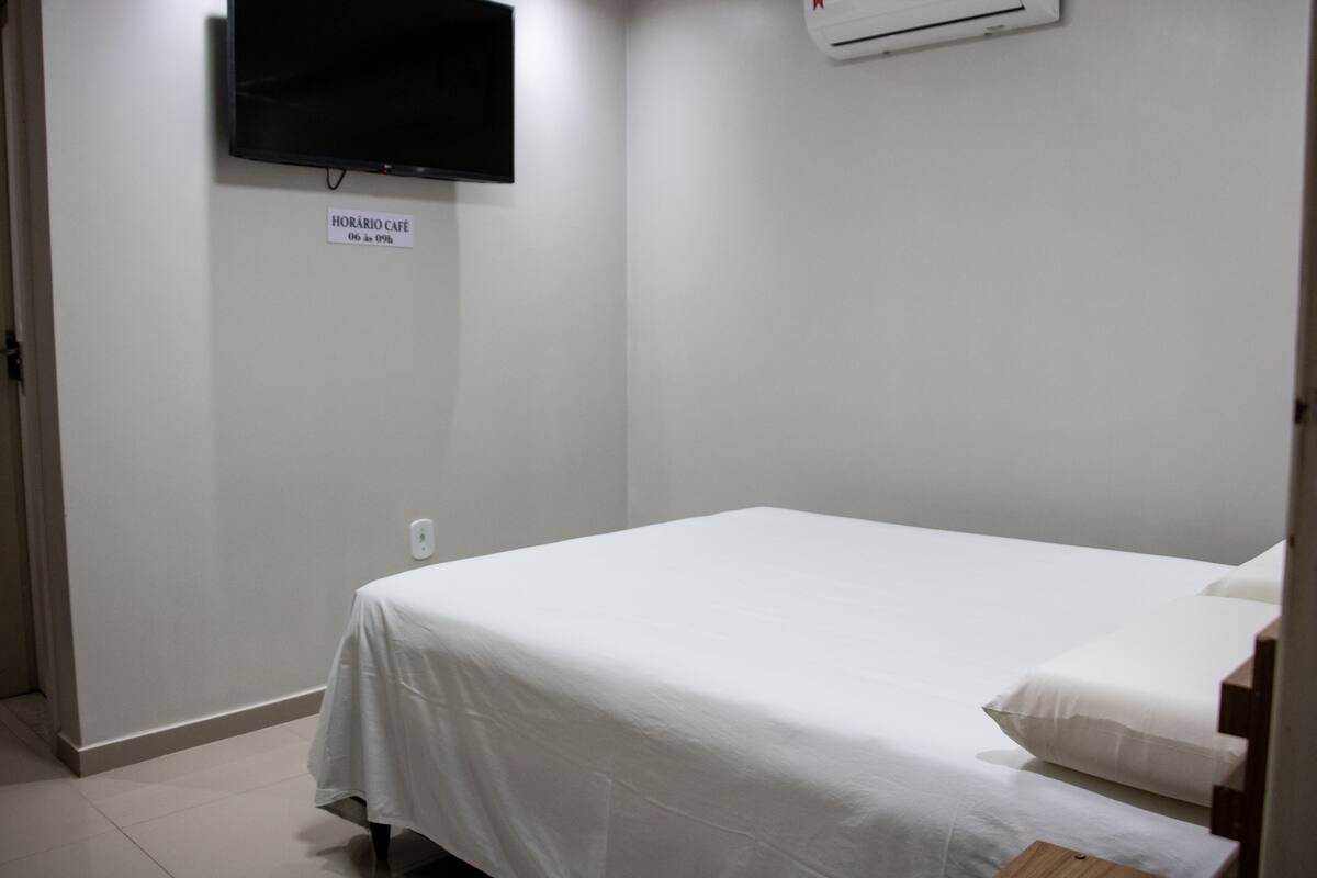 Una habitación pequeña y limpia con una cama individual, un televisor de pantalla plana montado en la pared, y un cartel que indica el nombre y el precio de la habitación.