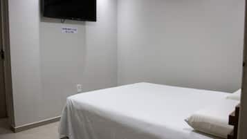 Una habitación pequeña y limpia con una cama individual, un televisor de pantalla plana montado en la pared, y un cartel que indica el nombre y el precio de la habitación.