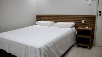 A neatly made bed with white linens, a wooden headboard, and a small bedside table with a remote control.