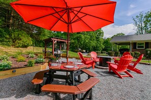 Enjoy al fresco dining under a shaded patio with a wooden table and Adirondack chairs.