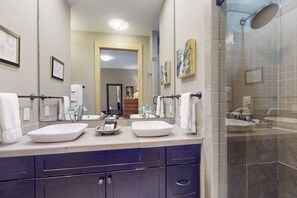 A modern bathroom with two sinks, a glass shower enclosure, and a mirror with artwork.