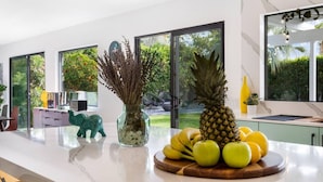 A modern kitchen with a marble countertop, a pineapple, bananas, and a vase of dried flowers. - Colorful Modern Luxury w/ Stunning Mountain Views (Palm Springs)