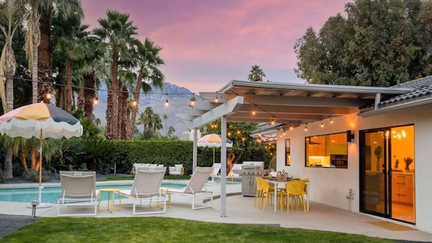 A modern outdoor patio with a pool, lounge chairs, and a dining area. - Colorful Modern Luxury w/ Stunning Mountain Views (Palm Springs)